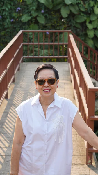 Aziatische senior vrouw die lacht met zonnebril op aard lopen houten dek — Stockfoto