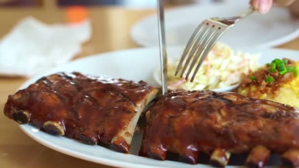 Video hands with knife and fork cutting baby pork ribs spare with barbecue sauce — Stock Video