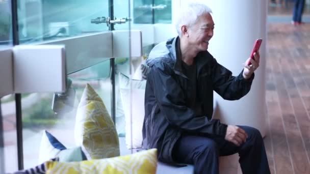 Homme âgé asiatique avec téléphone intelligent dans un bâtiment moderne. Les personnes âgées utilisant les nouvelles technologies pour rester connectées — Video