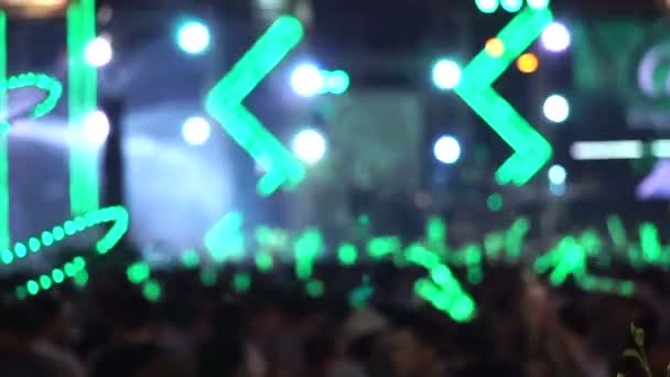 Multitud de personas disfrutando de un concierto al aire libre. Palillo de luz verde ondulante iluminado por luz verde colorida y aerosol de agua — Vídeos de Stock