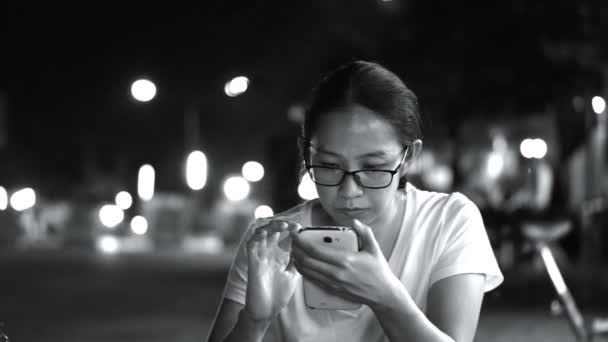 Preto e branco vidros ásia mulheres mensagens usando inteligente telefone com cidade no noite luz fundo — Vídeo de Stock