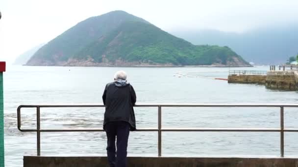 Asiatico senior uomo standing solo a il spiaggia anteriore molo in cupo pioggia giorno — Video Stock
