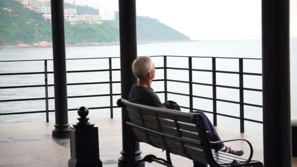 Asiatico senior uomo standing solo a il spiaggia anteriore molo in cupo pioggia giorno — Video Stock