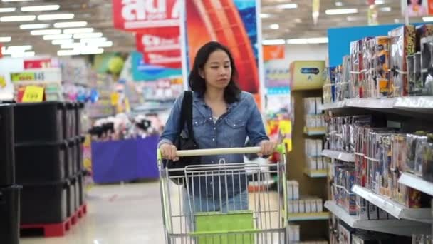 Chica asiática, mujer caminando, mirando y empujando el carrito de compras en la isla del supermercado — Vídeos de Stock