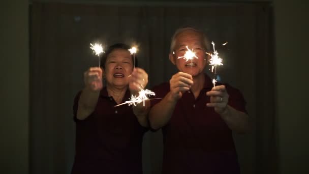 Ein asiatisches Seniorenpaar spielt Feuerwerk, Wunderkerzen, Feuerwerkskörper in der Nacht. Konzept feiert das Leben — Stockvideo