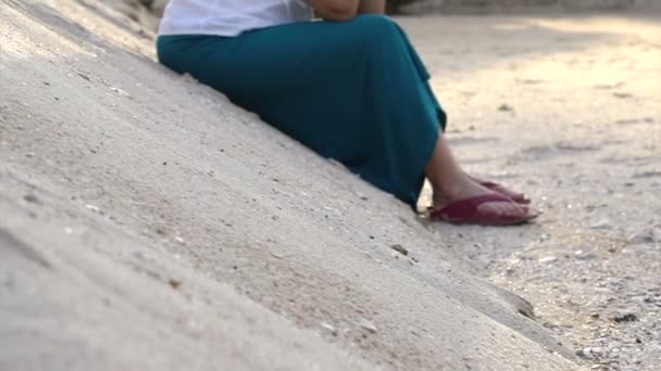 Asian senior woman sitting on sand dune at beach thinking about life — Stock Video