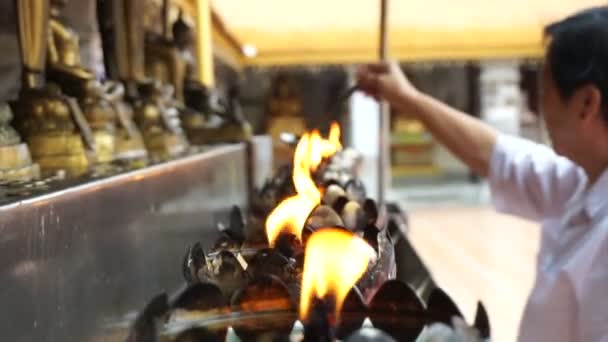 Asian senior doing Buddhist ritual pouring oil to fill candle frame for BUddha statue — Stock Video