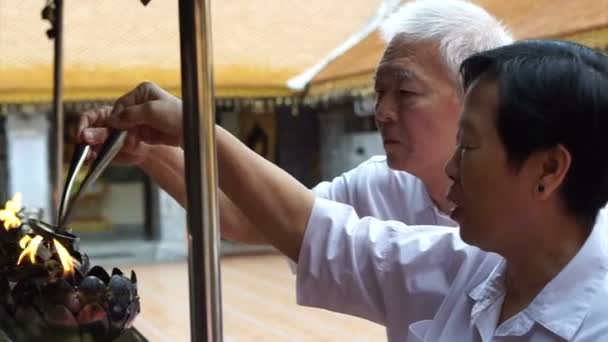 Asiatischer Senior bei buddhistischem Ritual, das Öl gießt, um Kerzenrahmen für Buddha-Statue zu füllen — Stockvideo