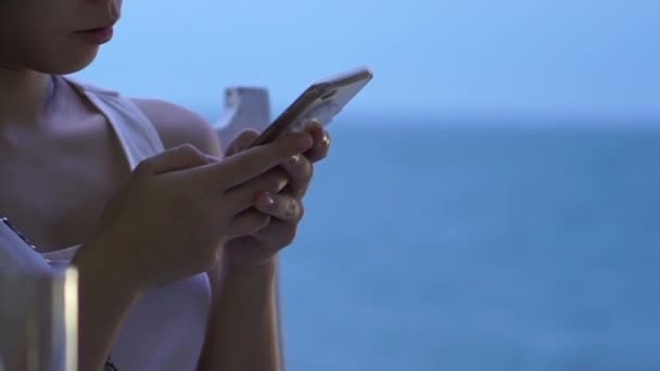 Aziatische vrouw met slimme telefoon tijdens schemering op blauwe oceaan strand — Stockvideo