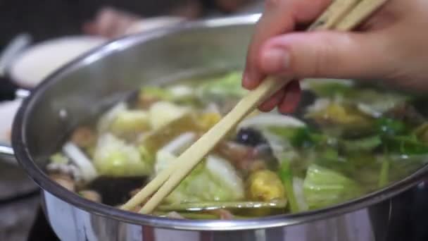 閉じる中国の澄んだスープ鍋魚介類と箸と手で食べる野菜 — ストック動画