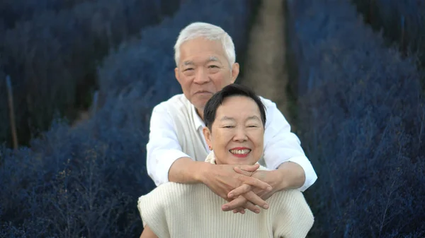 亚洲退休的老夫妇拥抱在迷人的蓝花地里庆祝爱情 — 图库照片