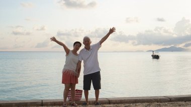Sahilde gün doğumu denizinde oynayan Asyalı yaşlı çift sabahın erken saatlerinde rahatlamış, mutlu bir emeklilik yaşadılar.