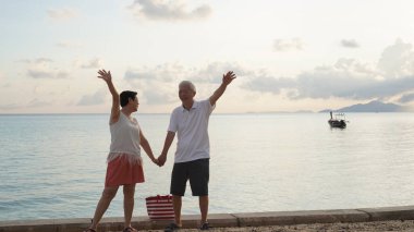 Sahilde gün doğumu denizinde oynayan Asyalı yaşlı çift sabahın erken saatlerinde rahatlamış, mutlu bir emeklilik yaşadılar.
