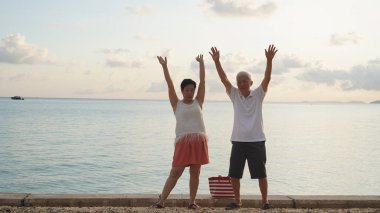 Sahilde gün doğumu denizinde oynayan Asyalı yaşlı çift sabahın erken saatlerinde rahatlamış, mutlu bir emeklilik yaşadılar.