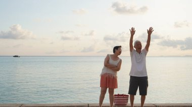 Sahilde gün doğumu denizinde oynayan Asyalı yaşlı çift sabahın erken saatlerinde rahatlamış, mutlu bir emeklilik yaşadılar.