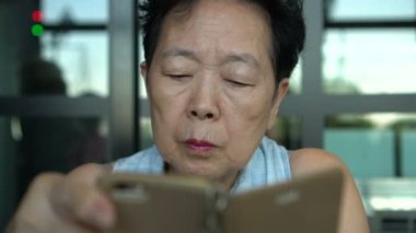 Asyalı kıdemli bir kadın sosyal medyada akıllı telefon sohbeti yapıyor.