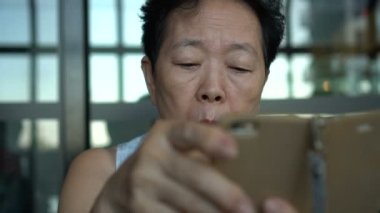 Asyalı kıdemli bir kadın sosyal medyada akıllı telefon sohbeti yapıyor.