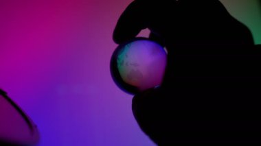 Hand holding transparent neon light globe ball control technonogy to help or destroy planet
