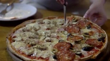 İtalyan ince biberli zeytinli pizza yarısı mantarlı jambon paylaşım için dilimleniyor.