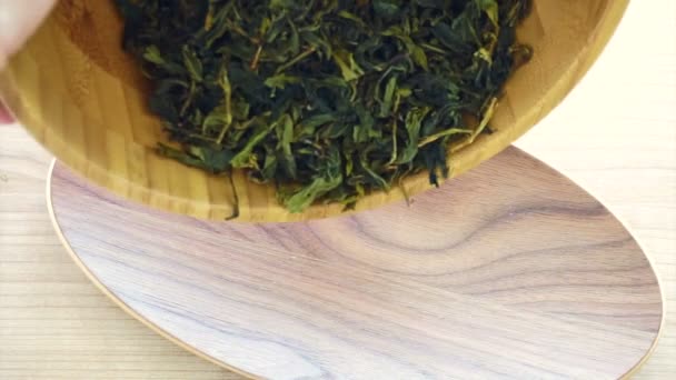 Лист сушеного чая, разливающийся в деревянную чашу на деревянном фоне — стоковое видео