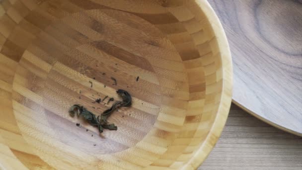 Gedroogde theebladeren gieten in houten kom op hout achtergrond — Stockvideo