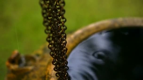 Wassertropfen fallen auf eine Metallkette, Regen läuft hinunter Link zu asiatischen Topf, um Wasser mit Abendlicht Unschärfe Hintergrund zu sammeln — Stockvideo