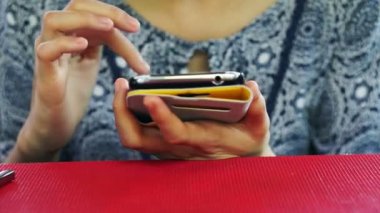 Asyalı kadın sarı büyük akıllı telefon kırmızı masada oynarken kullanarak