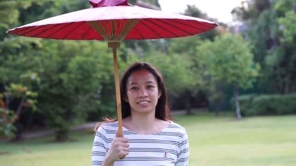 Asian girl with red oriental style umbrella on green nature background — Stock Video