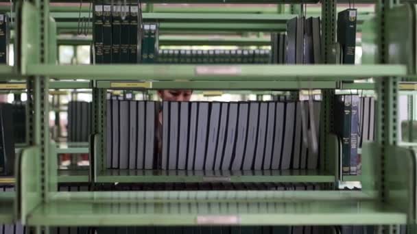 Vídeo de Mujer, estudiante caminando entre estantes, buscando libros en la biblioteca — Vídeos de Stock