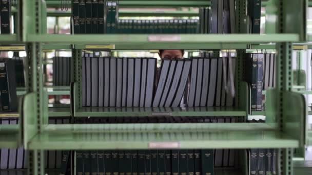 Vídeo de Mujer, estudiante caminando entre estantes, buscando libros en la biblioteca — Vídeos de Stock