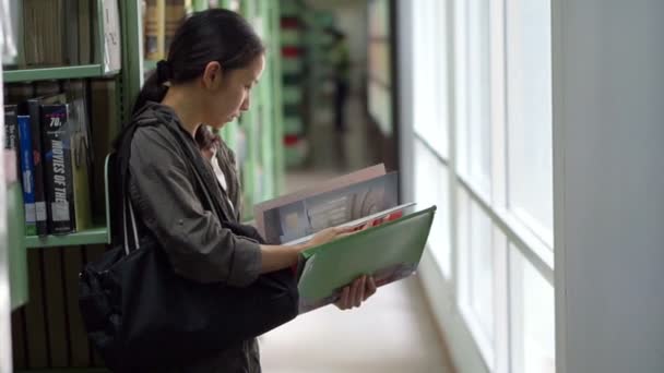 Mujer, estudiante de pie al lado de estanterías, lectura de libros biblioteca — Vídeo de stock