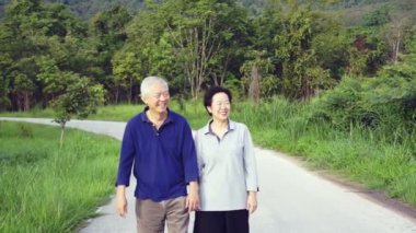 Mutlu Asya kıdemli video işaret, konuşurken çift ve dağ arka plan ile parkın içinden yürümek
