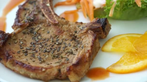 Vidéo de steak haché de porc grillé avec os. Salade colorée et sauce orange — Video