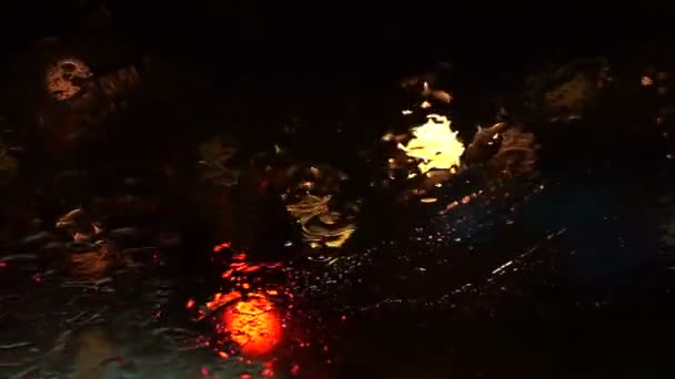 Video de la hermosa luz borrosa de colores del tráfico exterior en la carretera. Flujos de lluvia y limpiaparabrisas en el parabrisas delantero del coche — Vídeos de Stock