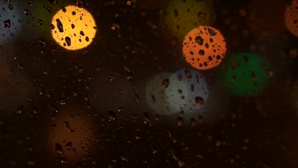 Video of beautiful colorful blurry light of traffic outside on the road. Rain flows and wipers on the car front windshield glass — Stock Video