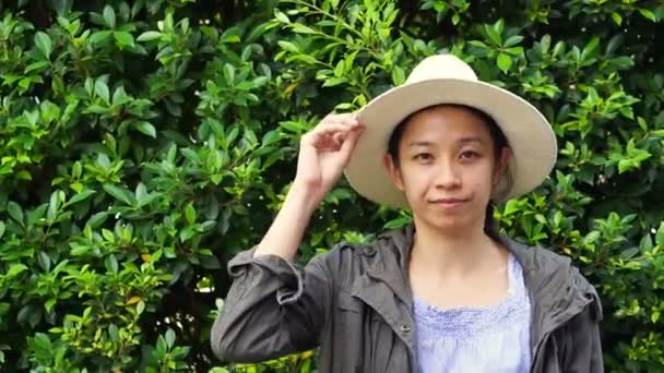 Video of Beautiful smiling Asian woman closeup portrait. Wearing hat with natural green bush background. modern life condominium — Stock Video