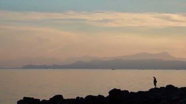 Videó az ember, a rock horgászhatnak a gyönyörű napfelkelte, silhouette: a tenger ocean — Stock videók