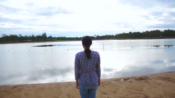 Видео азиатской девушки стоять прямо рядом с озером, на берегу моря — стоковое видео