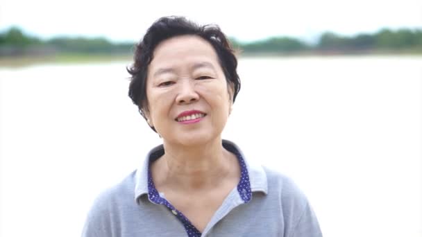 Vídeo de feliz asiático sênior mulher sorrindo feliz na frente da natureza lago — Vídeo de Stock
