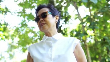 Güzel Asyalı üst düzey kadın güneş gözlüğü yeşil doğal arka plan üzerinde beyaz gömlek giyiyor