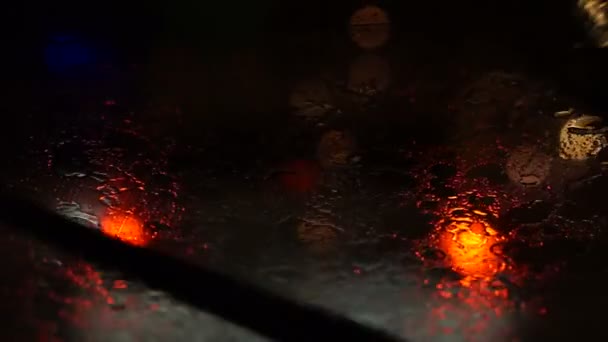 Video of beautiful colorful blurry light of traffic outside on the road. Rain flows and wipers on the car front windshield glass — Stock Video