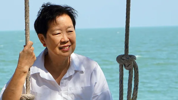 Asian senior woman playing swing with ocean ocean horizon backgr — Stock Photo, Image