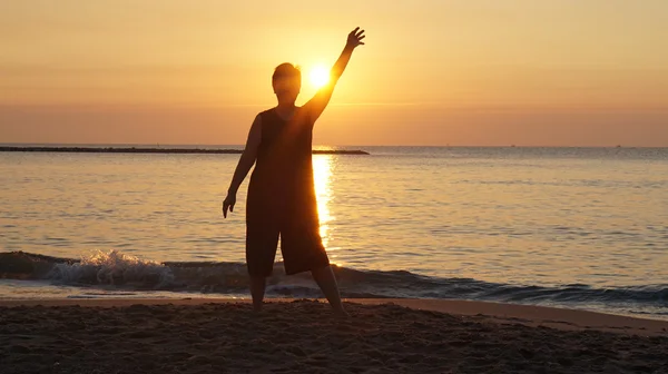 Senior woman silhouette raising hand in front of new day ornage — Stock Photo, Image