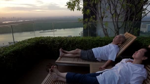 Ein asiatisches Rentnerpaar sitzt zusammen und betrachtet den Sonnenaufgang vom Dach aus. Gemeinsam abstraktes Lebensziel gesetzt — Stockvideo