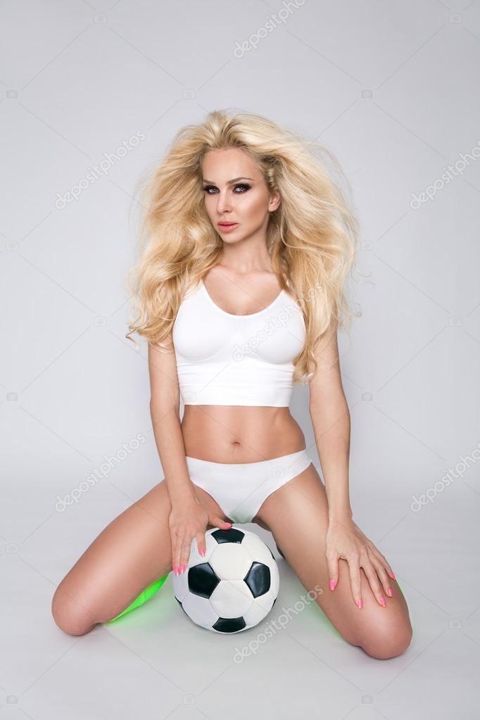 Beautiful young athletic girl blonde woman dressed in sports attire holding and playing football and joyfully smiles Stock Photo by ©marcink3333 111920278