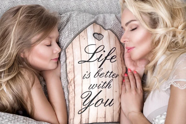 Portrait of the beautiful blonde woman mother and daughter on the beautiful face and amazing eyes lie sleeping on a bed i — Stock Photo, Image