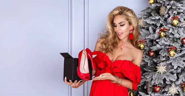 プレゼント箱を持った赤いドレスを着た陽気な女の子の肖像画と青い背景の上に隔離されたカメラを見て クリスマスのコンセプト — ストック写真