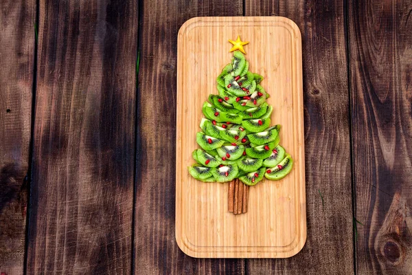 Kiwi Christmas tree - fun food idea for kids party or breakfast, New Year food on wooden background. Christmas tree food concept. Flat lay. Top view.