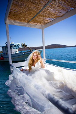 Beyaz elbiseli romantik gelin, arka planda dağlar ve deniz ile terasta poz veriyor. Santorini adasında gelin. Gelin, düğün konsepti.