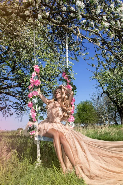 在花朵荡秋千上迷人的金发美女 春天的概念 美丽的自然女人 穿着雅致的粉色 淡淡的衣服 挂在花朵的秋千上 婚礼时尚和新娘的概念 — 图库照片